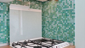 A kitchen with a gas stove, white cabinets, and green mosaic tiles.
