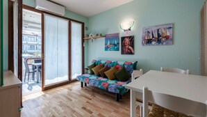A living room with a sofa, a dining table, and a view through a sliding glass door to an outdoor area.