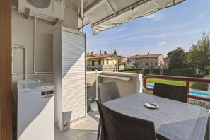A balcony with a table and chairs, a white appliance, and a view of houses and a swimming pool.