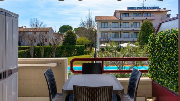 A terrace with a table and chairs, overlooking a swimming pool and Hotel Porto Azzurro.