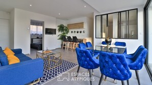 A modern living room with a sofa, blue chairs, and a dining area with a glass table and chairs. - Bandol Villa vue mer de 200 m² (Bandol)