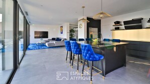 A modern kitchen with a central island, blue bar stools, and pendant lighting. - Bandol Villa vue mer de 200 m² (Bandol)