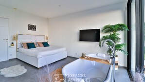 A modern bedroom with a large bed, a built-in bathtub, a TV mounted on the wall, and a potted plant. - Bandol Villa vue mer de 200 m² (Bandol)