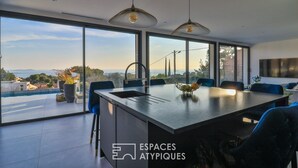 A modern kitchen with a large island, large windows, and a view of the city. - Bandol Villa vue mer de 200 m² (Bandol)
