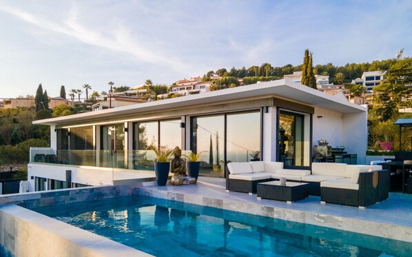 Ein modernes Haus mit Swimmingpool, Sitzgelegenheiten im Freien und großen Fenstern.