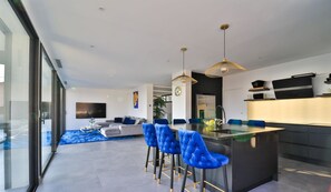Una cocina moderna con una isla central, taburetes azules y lámparas colgantes.