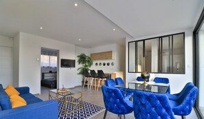 Una sala de estar moderna con un sofá, sillas azules y un comedor con una mesa de vidrio y sillas.