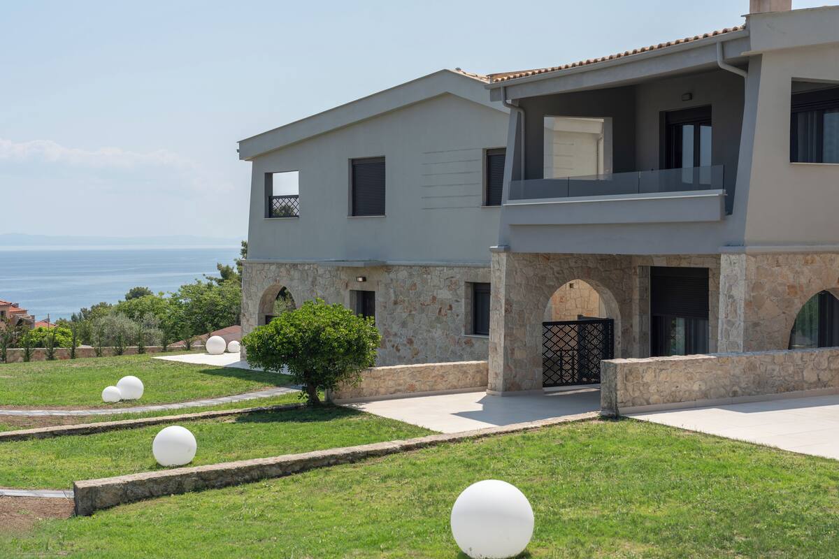 Une maison moderne à deux étages, dotée d’une façade en pierre, d’un balcon et offrant une vue sur la mer.