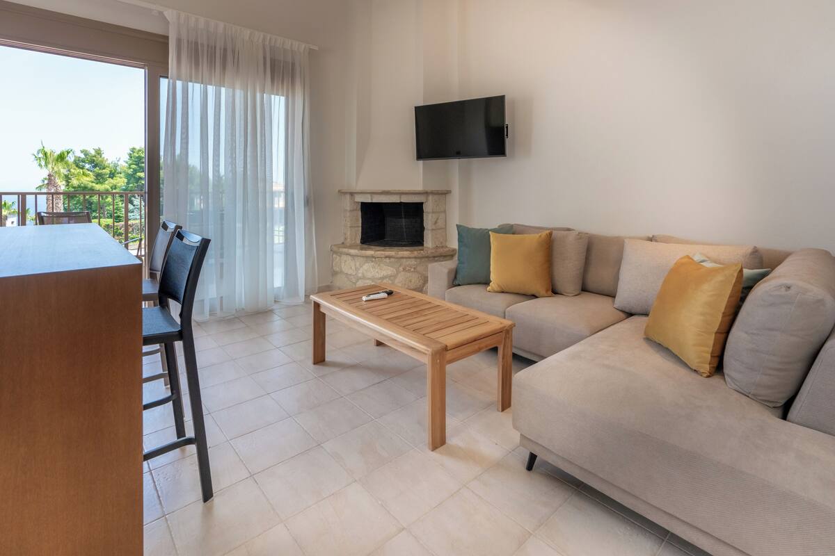 Un salon comprenant un canapé, une table basse, une cheminée, un téléviseur fixé au mur et un balcon avec une table et des chaises.