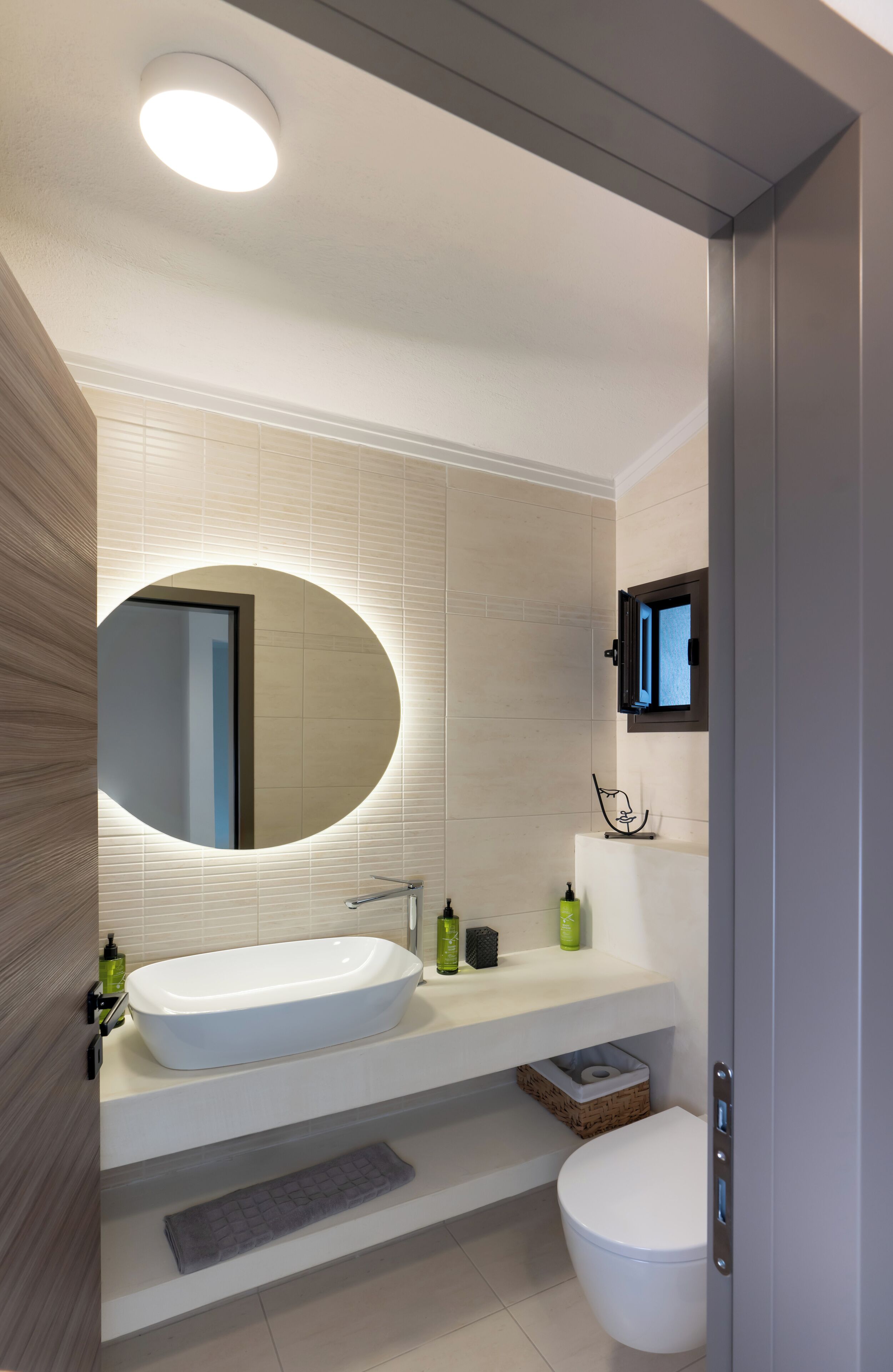A modern bathroom with a large oval mirror, a white sink, and a toilet.