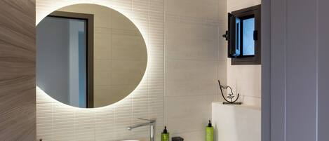 A modern bathroom with a large oval mirror, a white sink, and a toilet.