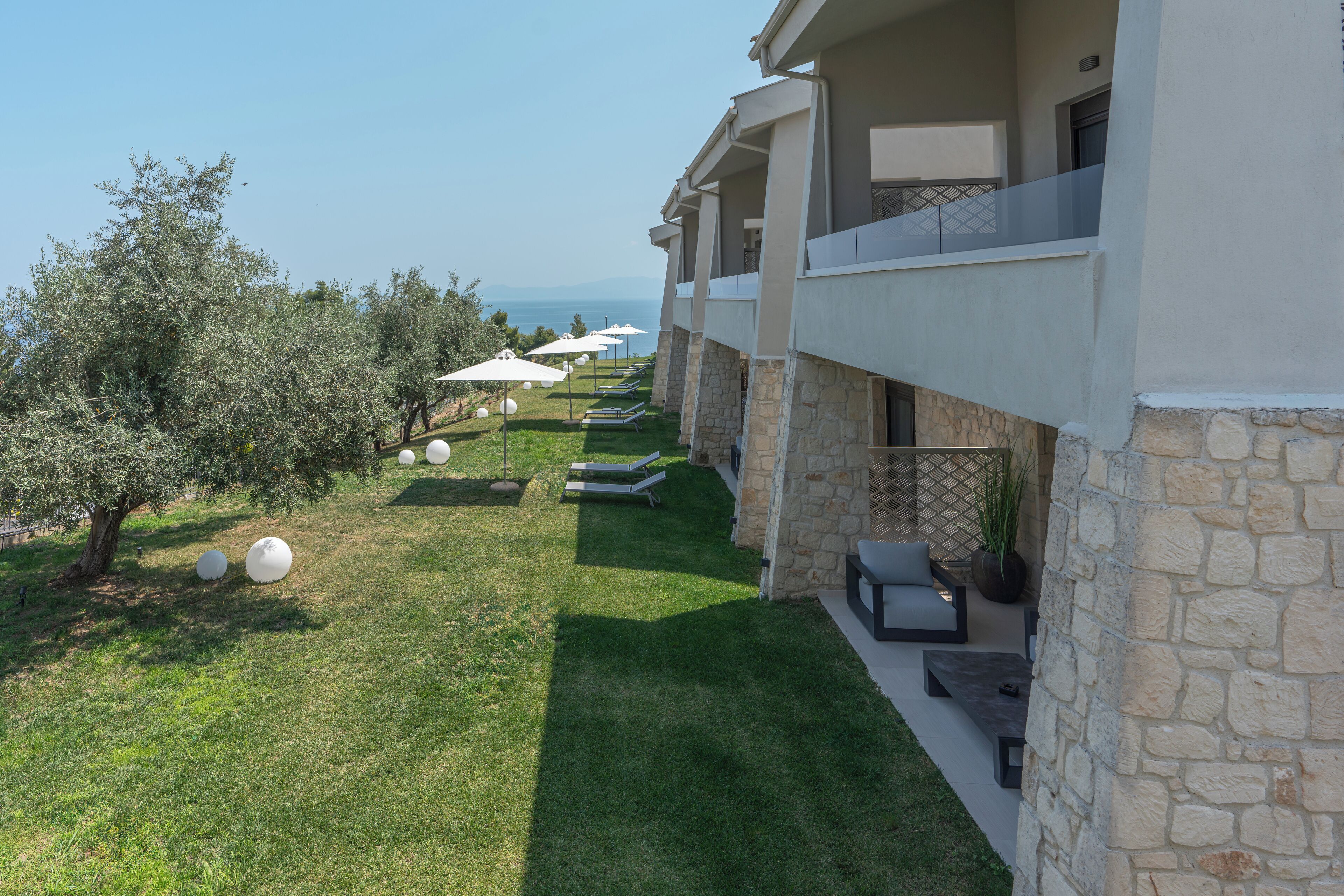 A hotel with a stone facade, outdoor seating, and umbrellas overlooking a grassy area with trees.