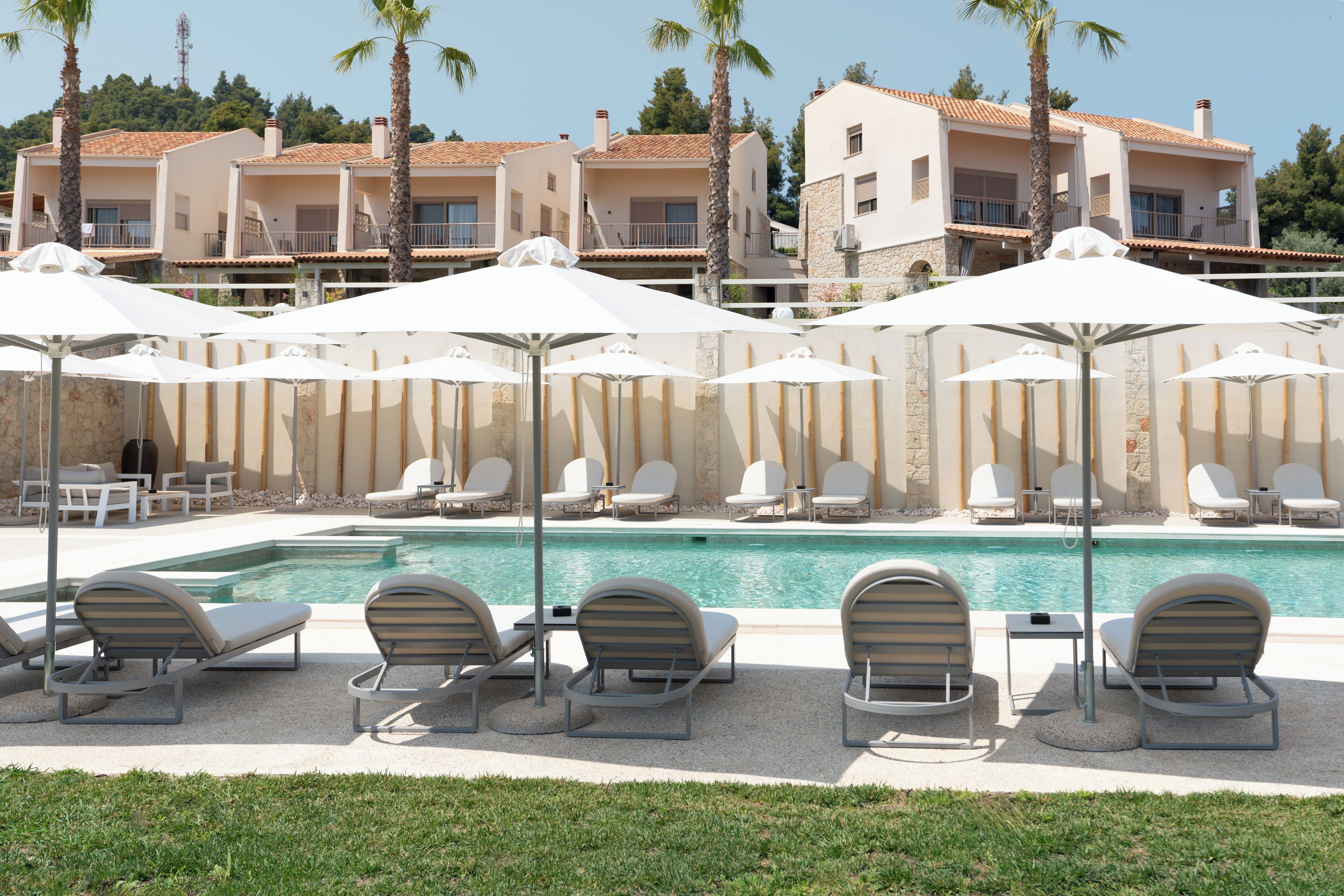 A poolside area with lounge chairs and umbrellas, a swimming pool, and a building with balconies in the background.