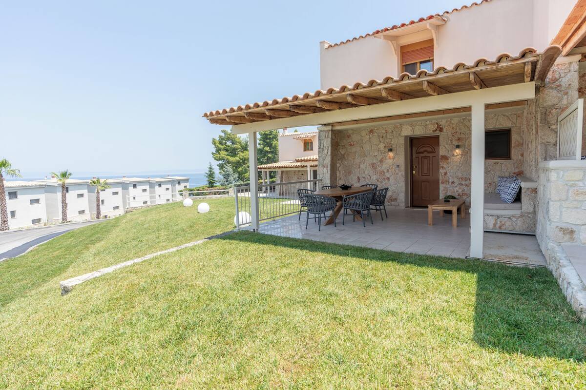 Un espace extérieur abrité, avec une table et des chaises, un mur en pierre et une vue sur la mer.