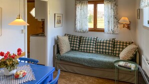 A cozy living room with a checkered sofa, a blue table with a vase of red flowers, and a window with floral curtains. - 2 bedroom awesome home in Löttörp (Löttörp)