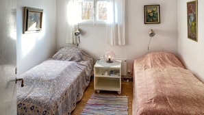 A small, cozy bedroom with two single beds, a bedside table with a lamp, a window with curtains, and a wall-mounted shelf. - 2 bedroom awesome home in Löttörp (Löttörp)