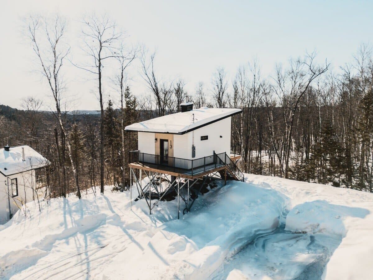 A cabin on stilts in a snowy landscape with a clear view of the surrounding forest.
