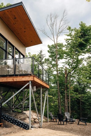 Une terrasse moderne en bois, dotée de rampes en verre, et entourée d’arbres.