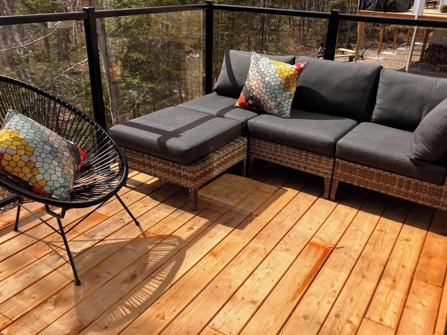 A wooden deck with a wicker sofa and a chair, both with grey cushions.