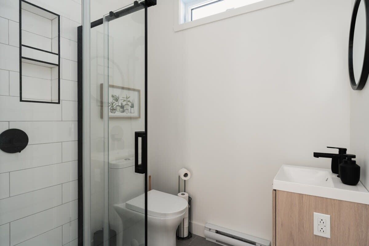 A modern bathroom with a glass shower enclosure, a white toilet, a sink with a black faucet, and a framed picture on the wall.