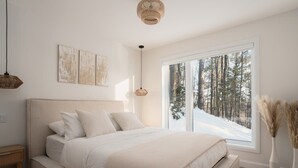 A bedroom with a large bed, a window with a view of trees, and a hanging light fixture.