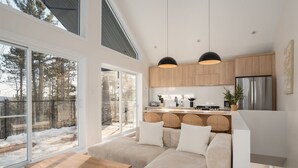 A modern kitchen with wooden cabinets, a stainless steel refrigerator, and a dining area with a wooden table and cushioned seating.