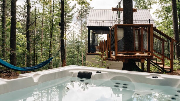 A hot tub surrounded by a forest, with a wooden deck and a metal structure in the background.