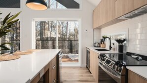 A modern kitchen with a large island, wooden cabinets, and a view of a snowy landscape through the glass door.