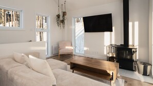 A modern living room with a sofa, a wooden coffee table, a TV mounted on the wall, and a black wood-burning stove.