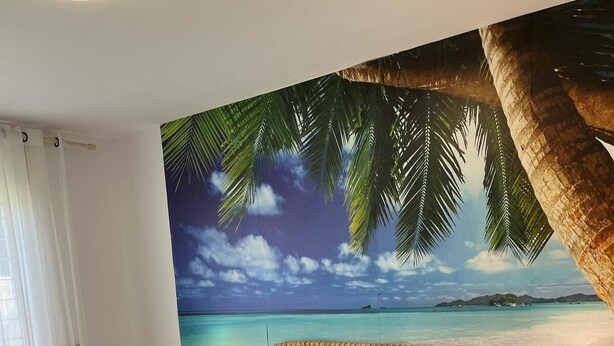 Une chambre à coucher avec un grand lit, deux tables de chevet et une fresque murale représentant une scène de plage.
