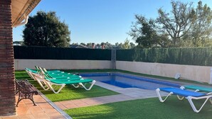 Un jardin avec une piscine, de l’herbe artificielle verte et des chaises longues.