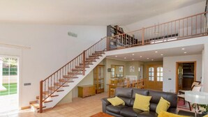 Un vaste espace de vie avec un escalier menant à l’étage supérieur, un canapé en cuir, une table basse en bois et, au fond, un coin repas.