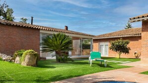 Un jardin avec une piscine, une maison en briques, une porte en verre et une pelouse verdoyante.