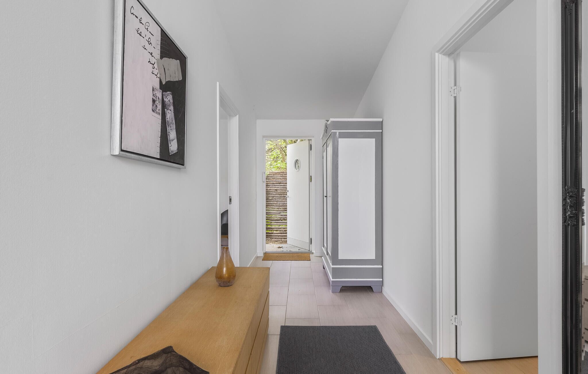 A hallway with a wooden bench, a framed picture on the wall, and a door leading to a room.