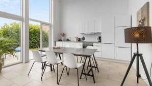 A modern kitchen with white cabinets, a dining table with four chairs, and a large window offering a view of greenery. - 2 bedroom gorgeous home in Gilleleje (Gilleleje)