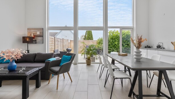 A modern living room with a large window, a dining area, and a kitchen. - 2 bedroom gorgeous home in Gilleleje (Gilleleje)