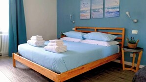 Ein ordentlich bezogenes Bett mit blauer Bettwäsche, einem hölzernen Kopfteil und einem kleinen Nachttisch mit einer Pflanze.