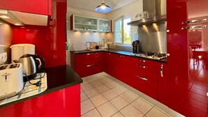 A modern kitchen with red cabinets, a gas stove, and a window providing natural light. - Carnac: 5-room house with garden, 7 people, WiFi, pets allowed (Carnac)