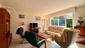 A living room with a sofa, a green armchair, a wooden cabinet, a television, and a floor lamp. - Carnac: 5-room house with garden, 7 people, WiFi, pets allowed (Carnac)