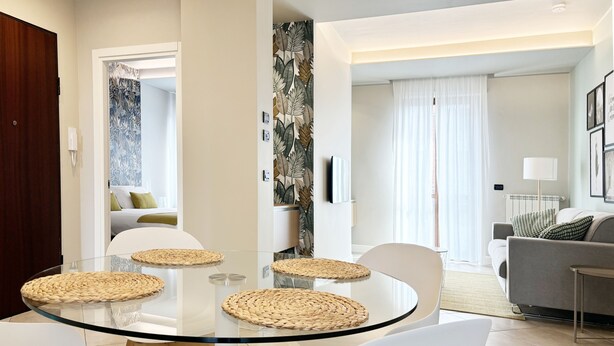 A modern living room with a glass dining table, white chairs, and a grey sofa. - **Lingotto Center** 5min, Luxury Apartment, 1 Bedroom, 4 guests. (Nichelino)