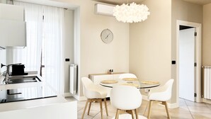 A modern kitchen with white cabinetry, a built-in oven, and a countertop with a kettle. There is a dining area with a round table and white chairs. - **Lingotto Center** 5min, Luxury Apartment, 1 Bedroom, 4 guests. (Nichelino)
