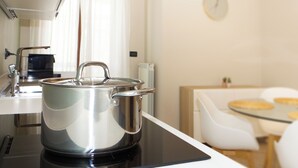 A modern kitchen with a stainless steel pot on an induction cooktop, a coffee maker, and a dining area with a glass table and white chairs. - **Lingotto Center** 5min, Luxury Apartment, 1 Bedroom, 4 guests. (Nichelino)