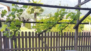 A patio with two wicker chairs and a small table, a wooden fence, and a view of a house and mountains in the background. - Apartment Weinduft (vine aromic) mountains beautyfull landscape (Appiano)