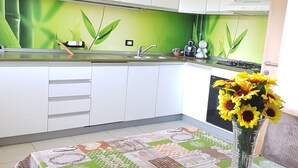 A kitchen with white cabinets, a green backsplash, and a table with a patchwork tablecloth. - Apartment Weinduft (vine aromic) mountains beautyfull landscape (Appiano)