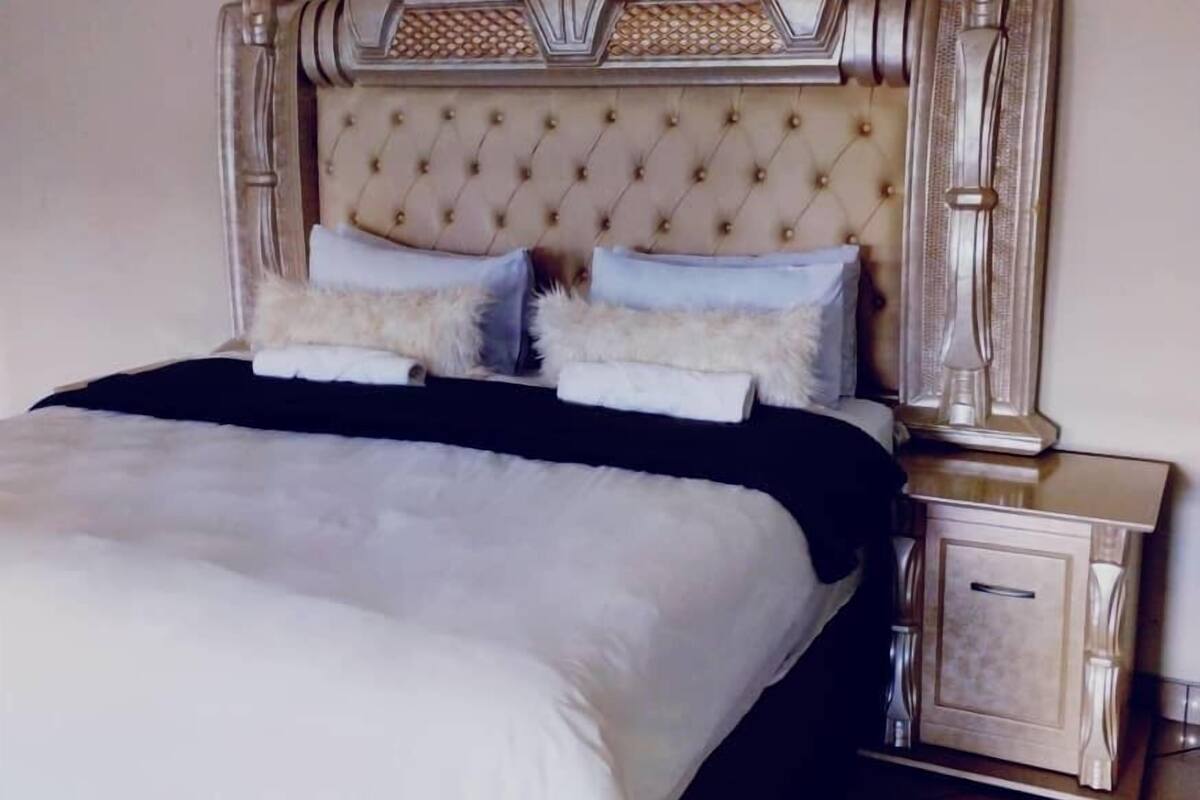 Una cama grande con cabecera capitonada, dos mesitas de noche y un buró.
