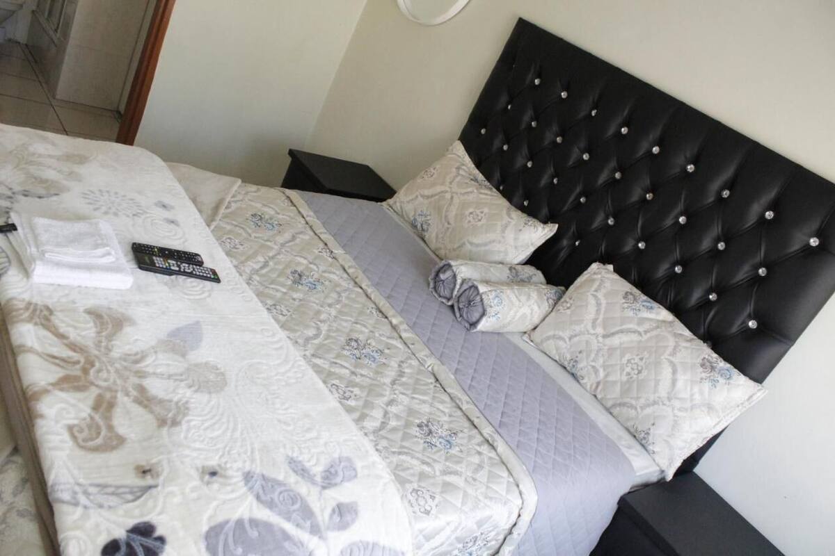 Una cama bien hecha con un edredón estampado de flores, un cabecero capitonado negro y un control remoto sobre la cama.