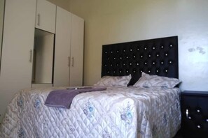 A bedroom with a bed, a headboard, a wardrobe, and a nightstand. - The Rest Camp Lodge (Manzini)