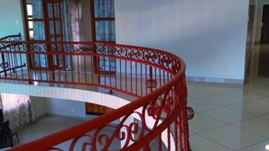 Amplio espacio interior con barandilla metálica roja, suelo de baldosas y vista a un edificio.