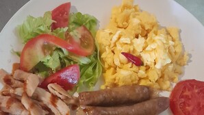 Un plato con huevos revueltos, salchichas, una rebanada de tostada, una ensalada con tomates y un trozo de pollo frito.