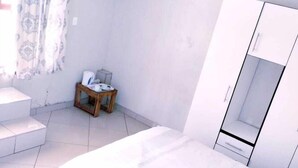 Un dormitorio con cama, armario, una mesita con silla y un aire acondicionado.